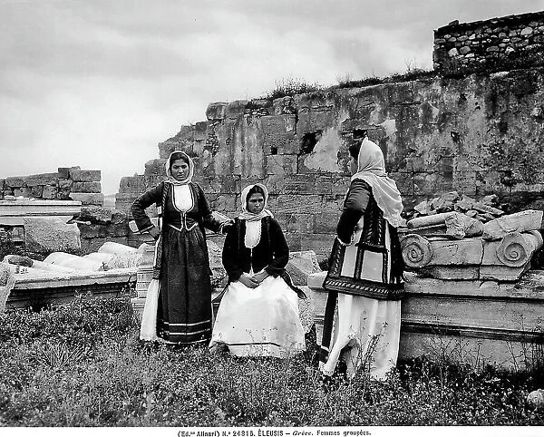 Portrait of three young women dressed in traditional costume, Eleusi. The ruins of old buildings are visible in the background