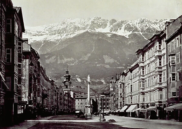 Theresienstrasse in Innsbruck, flanked by tall buildings. At the center is the eighteenth century column of Saint Anne. The snow-capped peaks of the Karwendel in the background