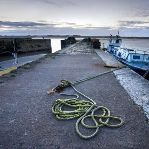 Beadnell Harbour at dusk showing old rope coiled on harbourside and dilapidated fishing boat