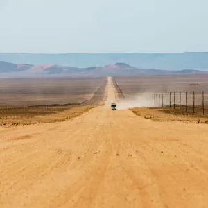 A jeep on a long sandy road in southern Namibia leaves a trail of dust, Namibia, Africa