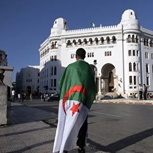 A man with an Algerian flag stands in front of Grande Poste in Algiers