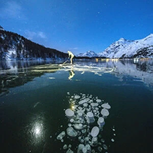 Full moon on ice skater on frozen Lake Sils lit by head torch, Engadine