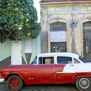 Old American car parked on street beneath fruit tree, Cienfuegos, Cuba