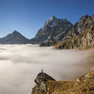 A clouds sea, in autumn, under Monviso peak and Viso Mozzo peak, with an alpinist on a pulpit rock