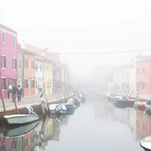 Colorful houses in Burano with canal and moored boats in the fog, Venice, Venetian lagoon