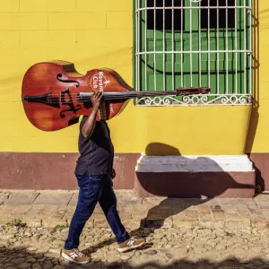 Musician with his double bass walking through the colourful street of Trinidad