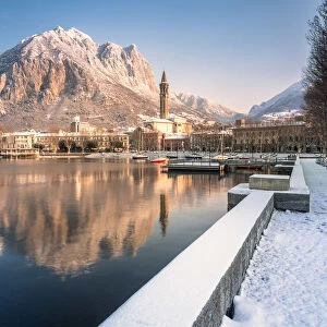 Snowy lakefront of Lecco and San Martino Mountain reflected in Como lake, Lecco province