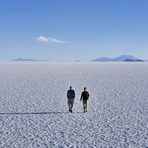 Two tourists walk across the endless salt crust of the Salar de Uyuni