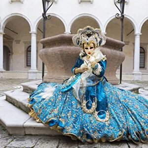 A woman sits in a magnificent costume in front of a well during the Venice Carnival
