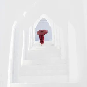 A young Buddhist monk holding a red umbrella walks up the steps in Hsinbyume Pagoda