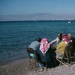 JORDAN, Aqaba Group of men playing backgammon on shore of beach with Eliat