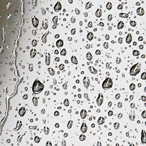 An airplane waiting to depart the gate is reflected in rain drops on a window at Logan