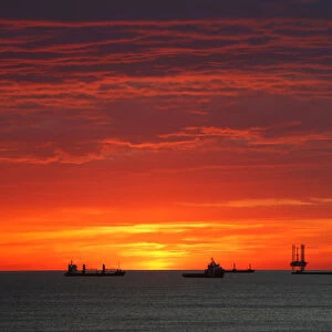 Cargo ships and an offshore supply vessel lie at anchor at sunrise off Sousse