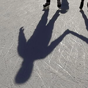 A couple casts shadows on the ice as they hold hands and skate on an outdoor rink