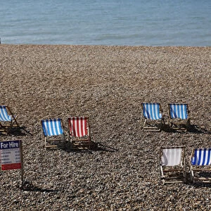 A couple sit on the beach near deck chairs in the sunny weather on Brighton beach