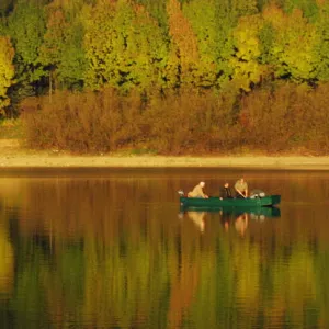 FISHERMEN IN BOAT ARE CAMOUFLAGED BY COLOURS OF FALL AT DAM IN SLOVAKIA