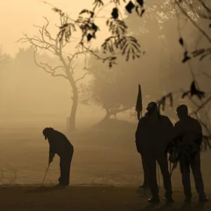 A golfer is silhouetted against the rising sun as he prepares to hit a shot during