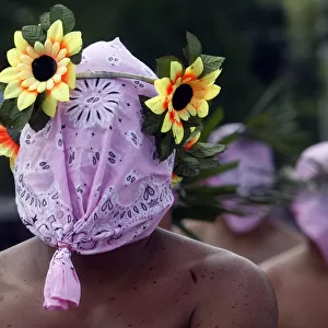 A hooded penitent wears an improvised crown made of plastic flowers during Maundy