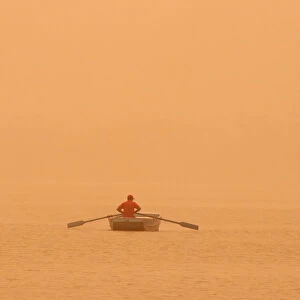 A man rows a boat amidst haze and dust in the waters of Sukhna lake in Chandigarh