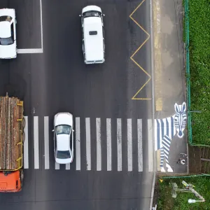 People wait at a zebra painted pedestrian crossing as vehicles drive along the R257