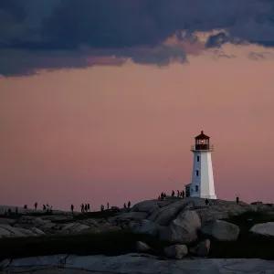 People walk on the rocks at the lighthouse at dusk in Peggys Cove