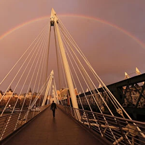 A rainbow appears as a pedestrian crosses one of the Golden Jubilee Bridges in London