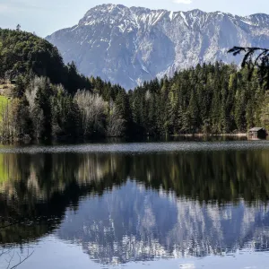 Snow covered mountains are reflected in Piburger lake on a sunny spring day in the