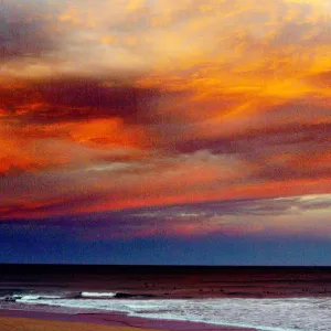 SURFER WALKS ALONG SYDNEY BEACH AT SUNSET