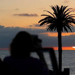 A tourist takes a picture of the setting sun at Moonlight Beach in Encinitas, California