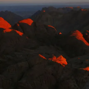 A tourist watches the sunrise and prays outside a church on the summit of Mount Moses