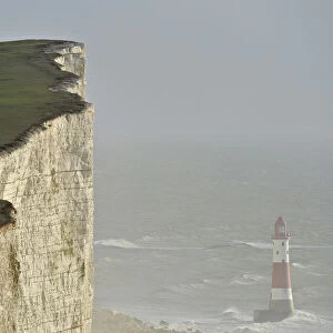 Walkers look out over Beachy Head lighthouse and heavy seas in the English Channel