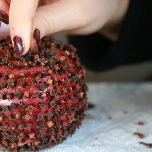 A woman decorates an apple with carnation seeds, which is a popular traditional gift