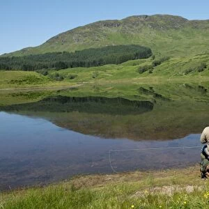 Angler sitting on shore of freshwater loch, Loch Lubhair, near Crianlarich, Trossachs, Stirling, Scotland, July