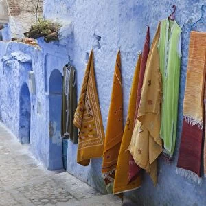 Blue houses and textiles for sale in alley of city, Chefchaouen, Morocco, april