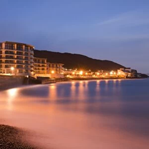 Sea rushing in over pebbles on beach below promenade in seaside resort before sunrise, Westward Ho