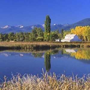 A white barn and beautiful fall foliage is reflected in pond at the Lee Metcalf National