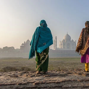 Women walking Mehtab Bagh, Moon Garden across from Taj Mahal in morning mist. Agra. India
