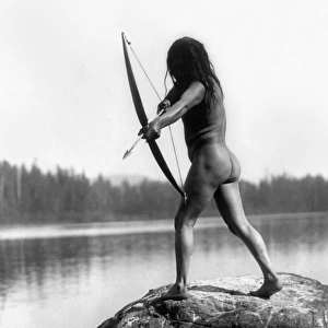 ARCHERY: NOOTKA INDIAN. A nude Nootka Indian bowman taking aim into the water, Pacific Northwest Coast. Photographed by Edward S. Curtis, c1910