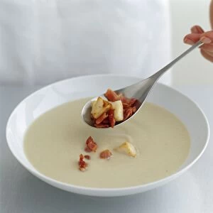 Bacon and scallop garnish added to cream soup with spoon, close-up