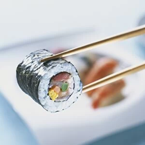 Futo maki zushi, cylindrical sushi parcel up held with chopsticks, close-up