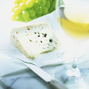 A glass of white wine and a dish of white grapes and Roquefort cheese with cheese knife