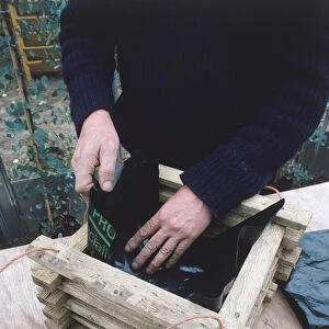 Man making a wooden hanging basket lining it with strips of polythene