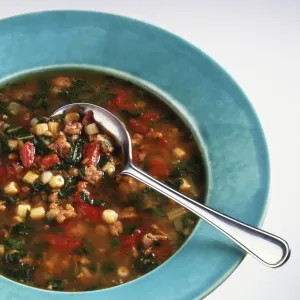 Minestrone soup made with lentils, salsiccia sausage, chard and pasta, served in blue bowl, with spoon