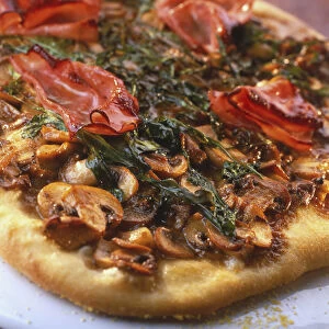 Round pizza with medium-thick, crispy crust, topped richly with sliced mushrooms, ham and rocket, close up, tilted view