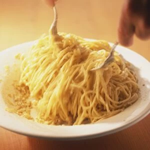 Spaghetti being tossed in a cream sauce with two forks