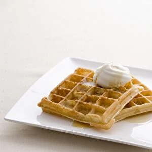 Waffles served with maple syrup and dollop of ice cream on rectangular white plate, close-up