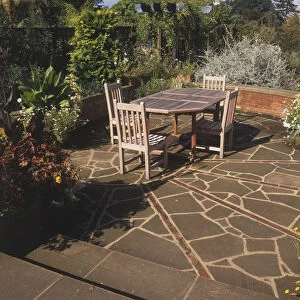 Wooden garden table and four chairs on a patio, floor made of asymmetric paving stones