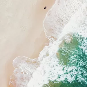 An aerial beach shot of guy walking on the beach and the waves breaking on the shore