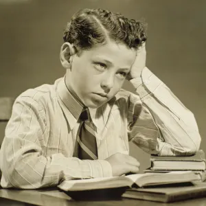 Boy (10-11) sitting at table over open book, head resting on hand, (B&W), close-up