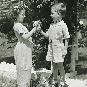 Boy (4-5) giving girl (4-5) flowers, (B&W)